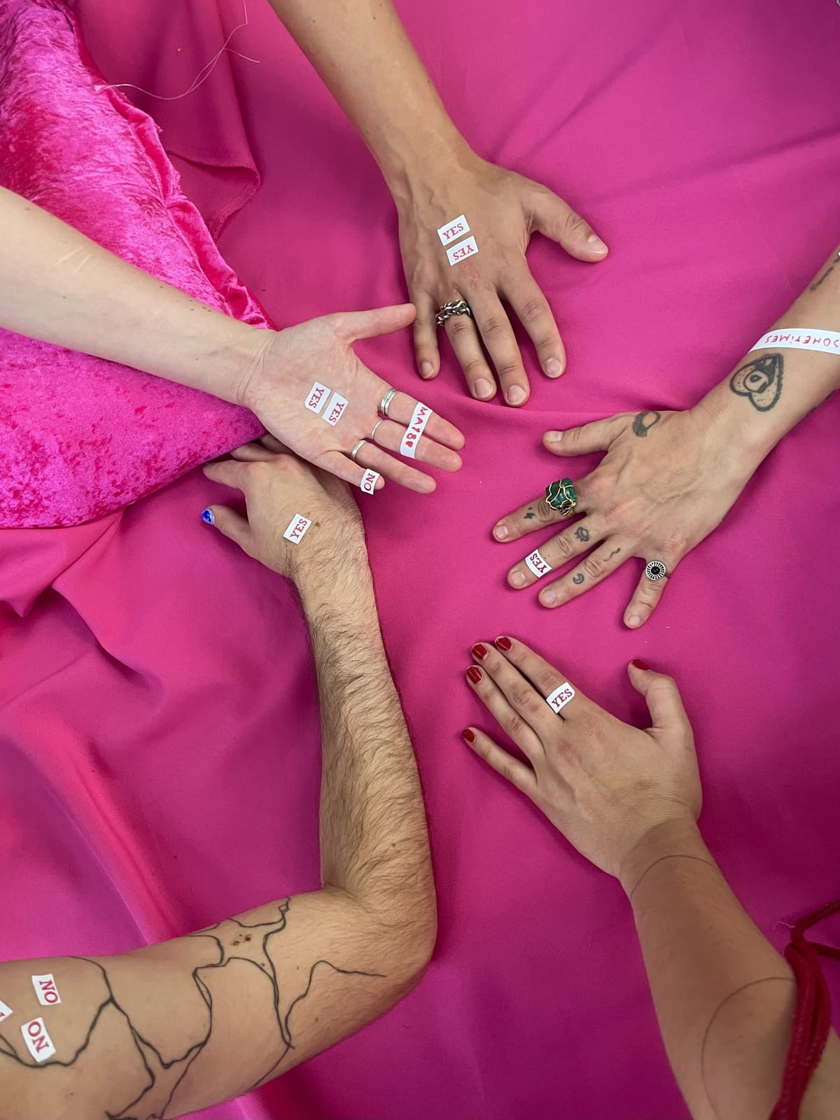 Five hands on pink fabric, with small YES, NO and MAYBE stickers on fingers and wrists